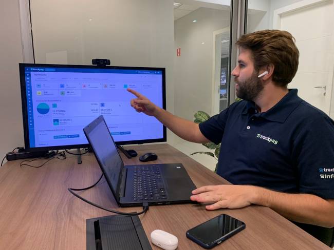 Kassio Seefeld, CEO da TruckPag, apontando para monitor mostrando a dashboard do TruckPag Bank